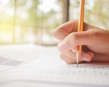 hand student testing in exercise and taking fill in exam carbon paper computer sheet with pencil at school test room, education concept